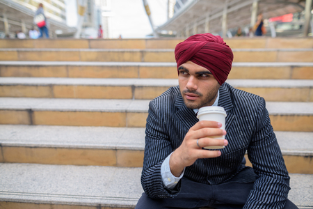 Indian businessman sitting outdoors in city while holding coffee cupの写真素材