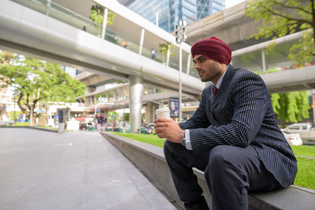 Indian businessman sitting outdoors in city while having coffee breakの写真素材
