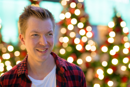 Young Happy Man Smiling And Thinking Against Christmas Trees Outdoorsの写真素材
