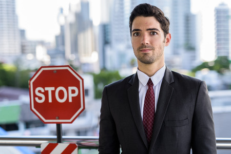 Portrait of young businessman standing next to STOP signの写真素材