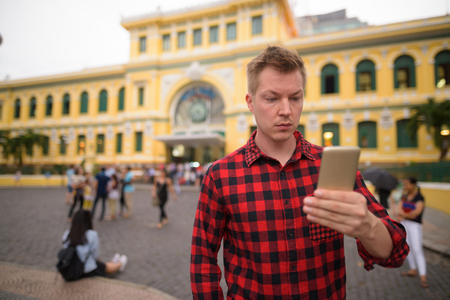 Tourist man using phone in front of Saigon Central Post Officeの写真素材