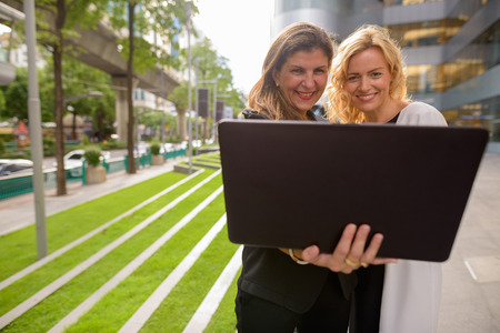 Portrait of two happy businesswoman using laptop computer together outdoorsの写真素材