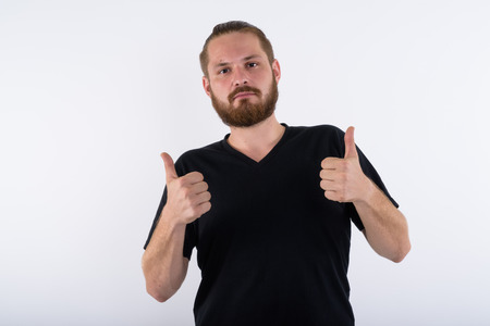 Studio shot of young bearded man giving thumbs up against whiteの写真素材