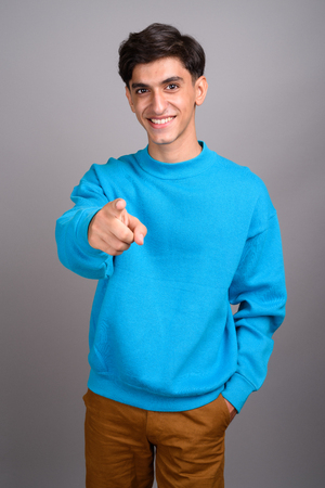 Young happy Persian teenage boy smiling and pointing finger at cameraの写真素材