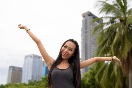 Young beautiful Asian woman relaxing at the park with arms raised