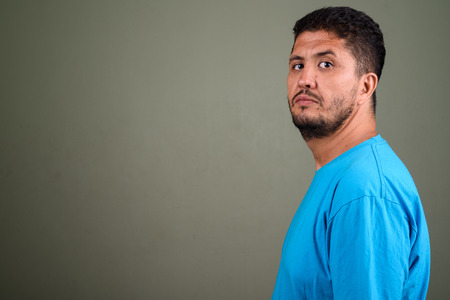 Bearded Persian man wearing blue shirt against colored backgroun