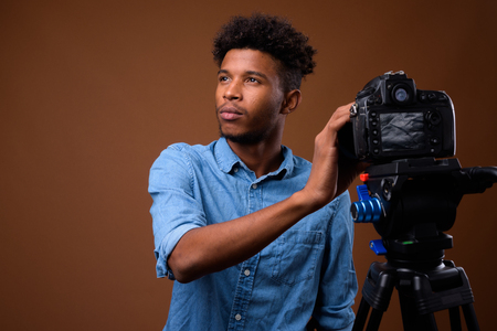 Young handsome African man vlogging with DSLR camera in studio