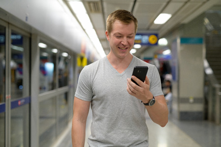 Young happy tourist man using phone at the underground train station in Bangkok