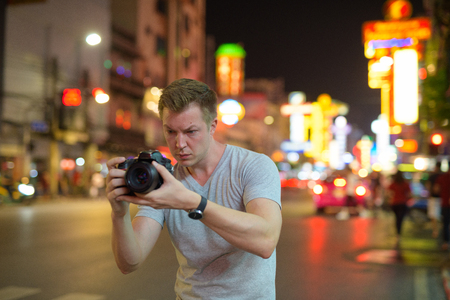 Young tourist man photographing with camera in the streets of Chinatown at nightの写真素材