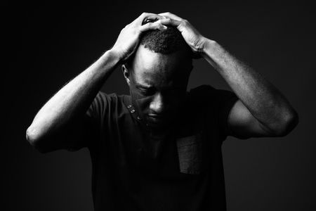 Sad young African man against black background in black and whiteの写真素材