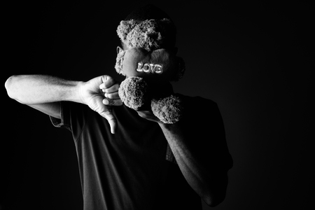 Sad young African man with teddy bear and love sign text giving thumb downの写真素材