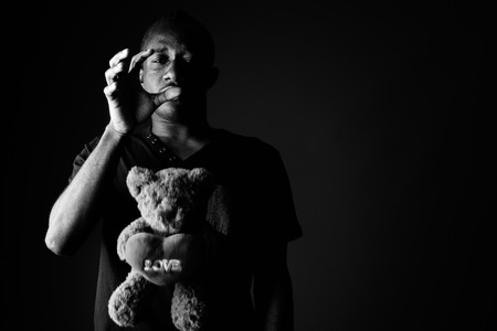 Sad depressed young African man with teddy bear and love sign text in black and whiteの写真素材