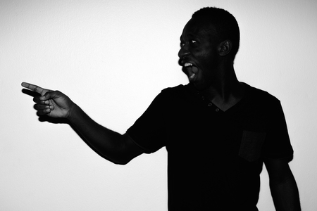 Studio shot of young African man wearing black shirt against white background in black and whiteの写真素材