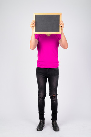 Full body shot of young man showing blackboard and covering faceの写真素材