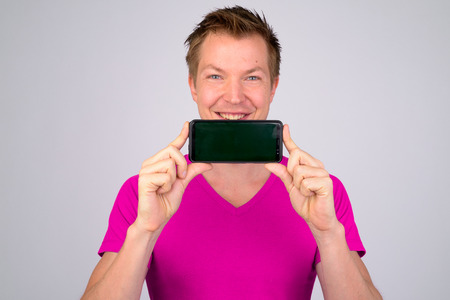 Face of happy young handsome man smiling while showing phoneの写真素材