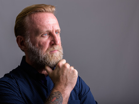 Studio shot of mature bearded man with hand tattoos thinkingの写真素材