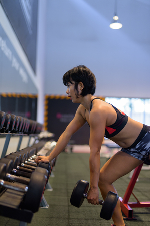 Young beautiful Asian woman doing dumbbell row in gymの写真素材