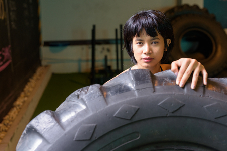 Asian fitness woman pushing and flipping wheel truck tire at gymの写真素材