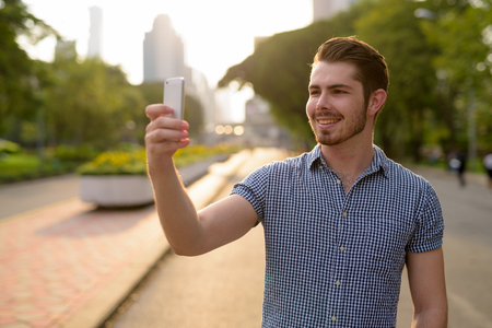 Happy man relaxing at the park while using mobile phoneの写真素材