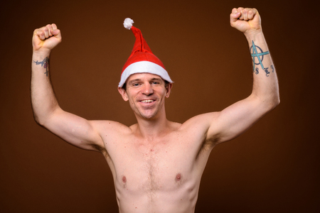 Shirtless man wearing Santa hat ready for Christmas against browの写真素材