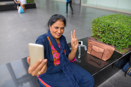 Mature Indian woman taking selfie with mobile phone in cityの写真素材