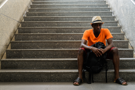 Young black African tourist man sitting on stairsの写真素材