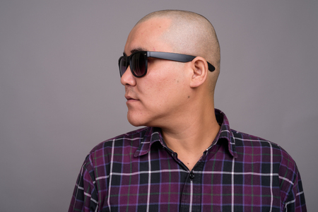 Young bald Asian businessman against gray backgroundの写真素材