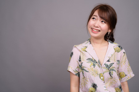 Portrait of young happy Asian tourist woman smiling and thinkingの写真素材