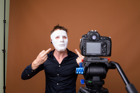 Young man wearing mask while vlogging and showing middle fingerの写真素材
