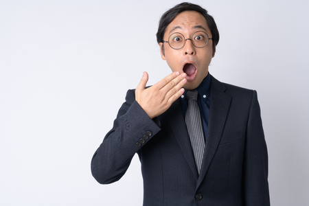 Portrait of shocked Japanese businessman in suit covering mouthの写真素材