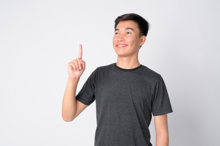 Portrait of young happy Asian man thinking and pointing upの写真素材