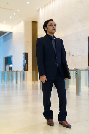 Full body shot of Asian businessman walking with laptopの写真素材