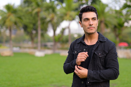 Young handsome Hispanic man thinking in the park outdoors