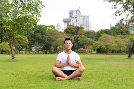 Young handsome Hispanic man meditating with eyes closed at the parkの写真素材