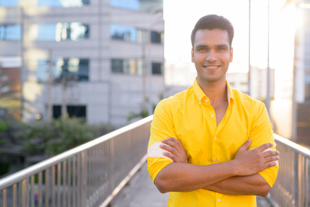 Happy young handsome Indian man smiling with arms crossed on the footbridgeの写真素材