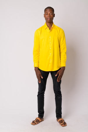 Full body shot of young handsome bald African businessman wearing yellow shirtの写真素材