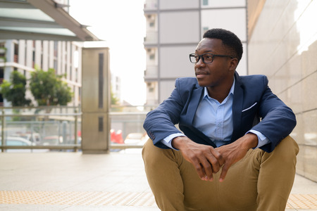Young thoughtful African businessman sitting outside the subway train stationの写真素材