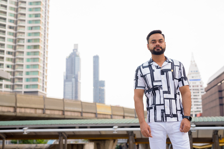 Young bearded Indian man against view of sky train stationの写真素材