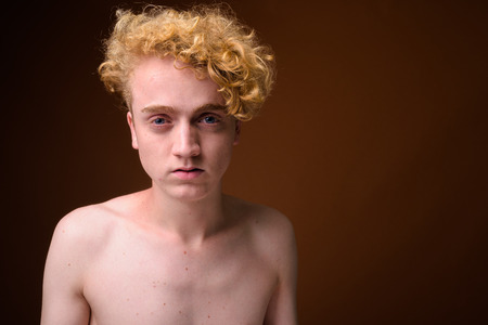 Skinny young man with curly hair shirtless against brown backgroの写真素材