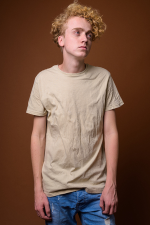 Skinny young man with curly hair against brown backgroundの写真素材