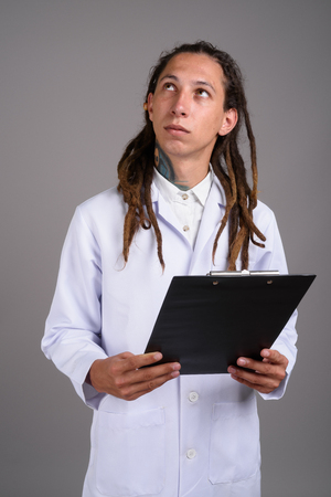 Young man doctor with dreadlocks against gray backgroundの写真素材