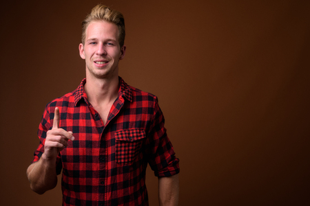 Studio shot of young handsome man against brown backgroundの写真素材