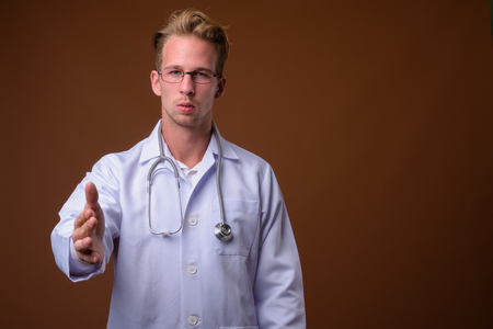 Young handsome man doctor against brown backgroundの写真素材
