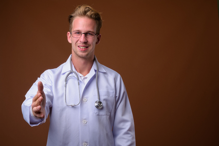 Young handsome man doctor against brown backgroundの写真素材