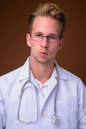 Young handsome man doctor against brown backgroundの写真素材