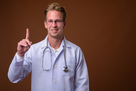 Young handsome man doctor against brown backgroundの写真素材