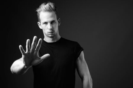 Studio shot of young handsome man against gray background in blackの写真素材