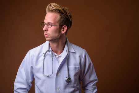 Young handsome man doctor against brown backgroundの写真素材