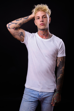 Studio shot of young handsome rebellious man with blond hair against black backgroundの写真素材