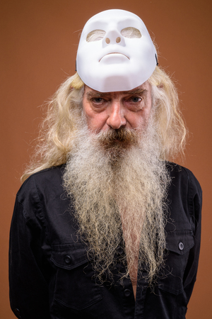 Portrait of senior bearded man holding white maskの写真素材
